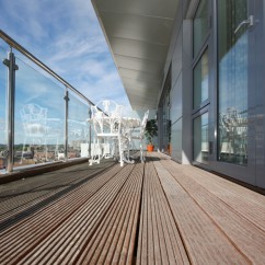 Longue terrasse en composite avec garde-corps en verre, table et chaises en fer forgé blanc