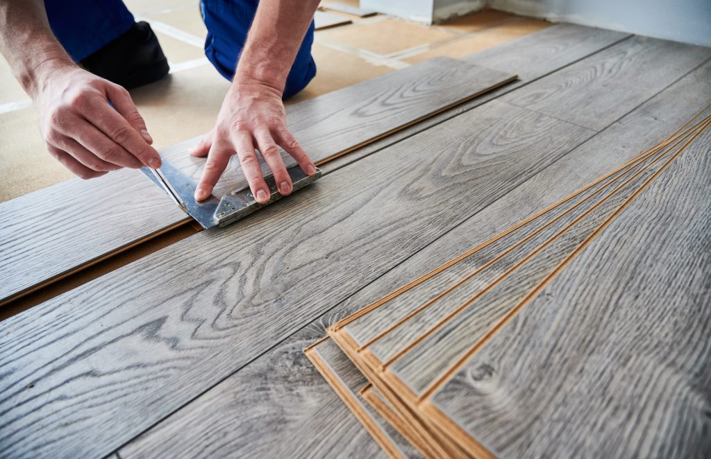 Personne agenouillée qui taille des lattes de vinyle pour plancher 