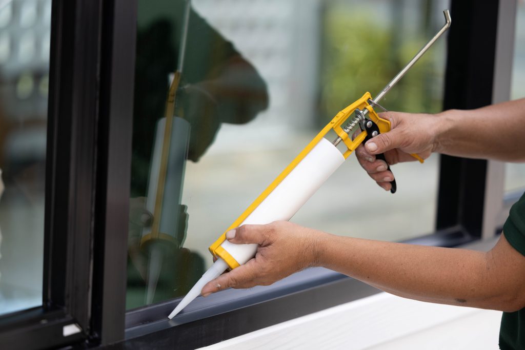 Personne qui utilise un pistolet de calfeutrage en silicone pour remplir une fuite dans une fenêtre de maison