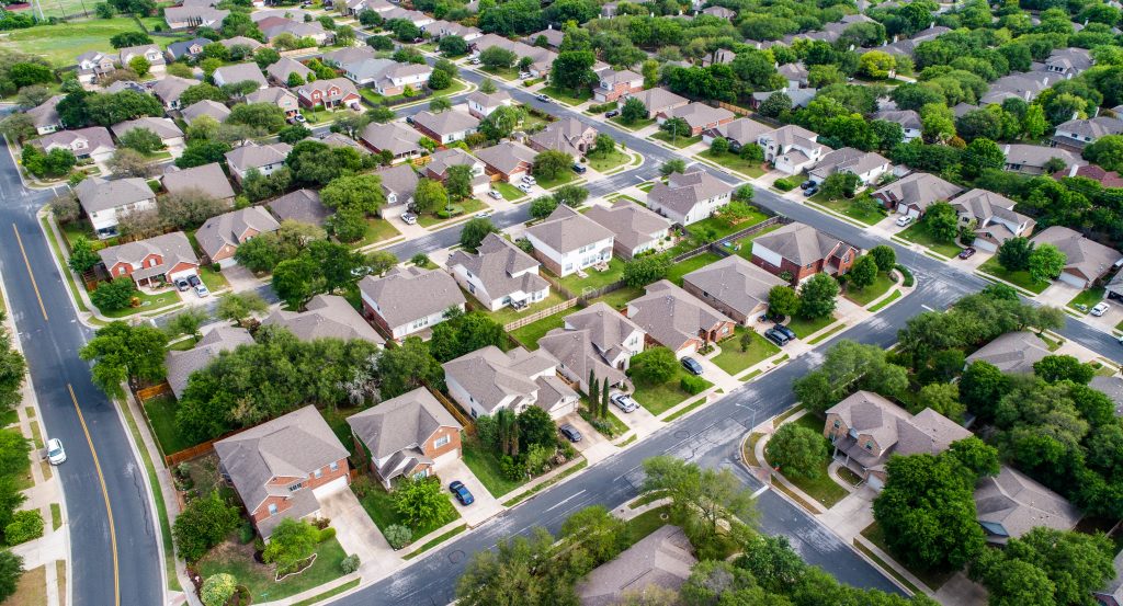 Aerial view of a suburb, with single-family homes, grassy lawns, and trees 