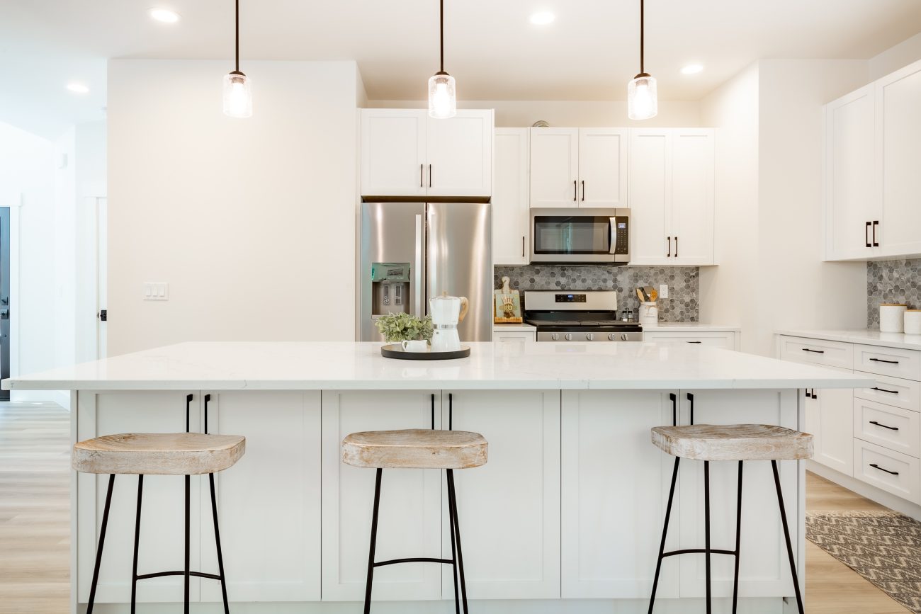 Cuisine moderne blanche avec îlot, tabourets, dosseret en carrelage, appareils électroménagers en inox et plancher en bois