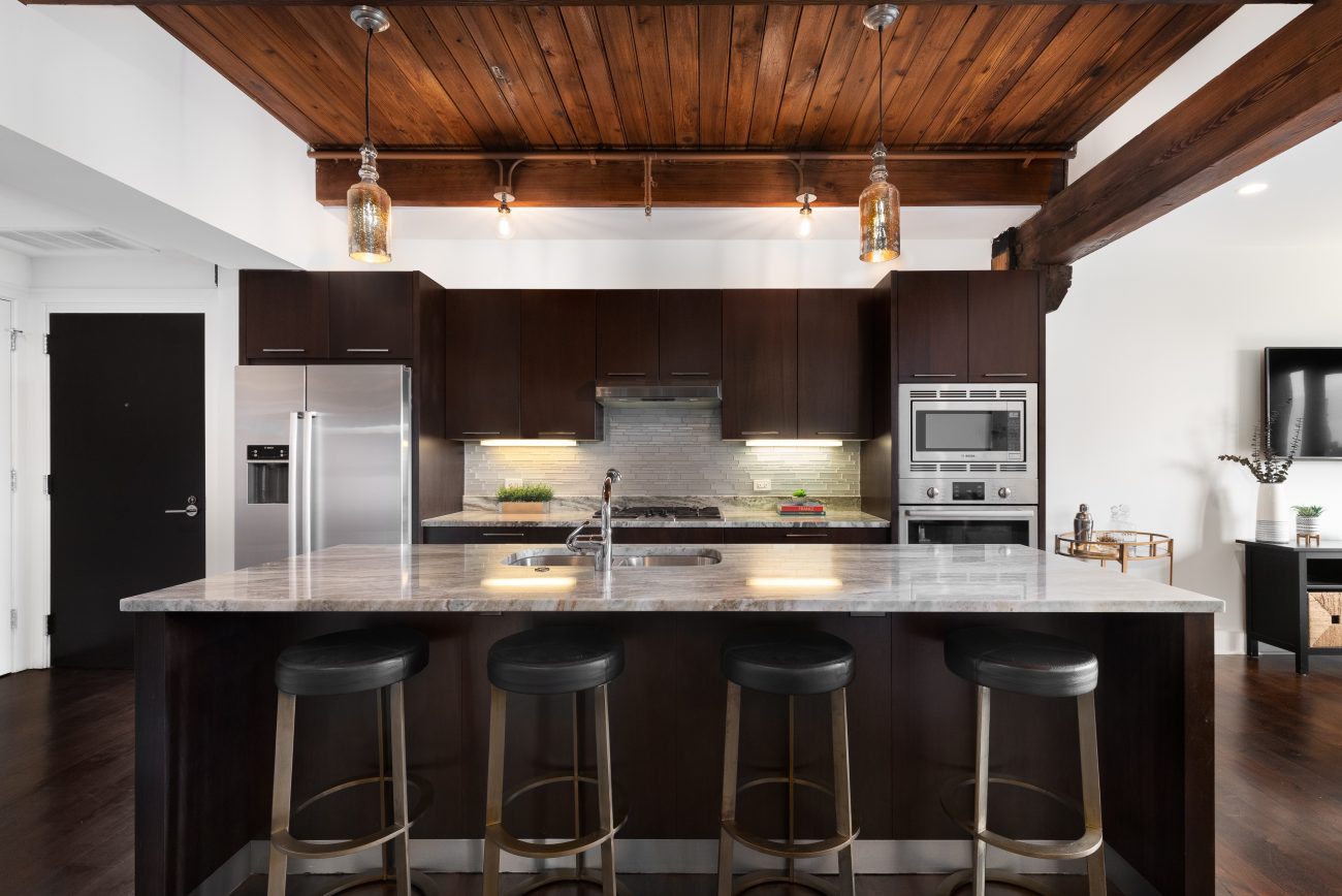 Modern kitchen in dark mahogany with bar stools in front of the island, glass pendant lights, wood-covered ceiling