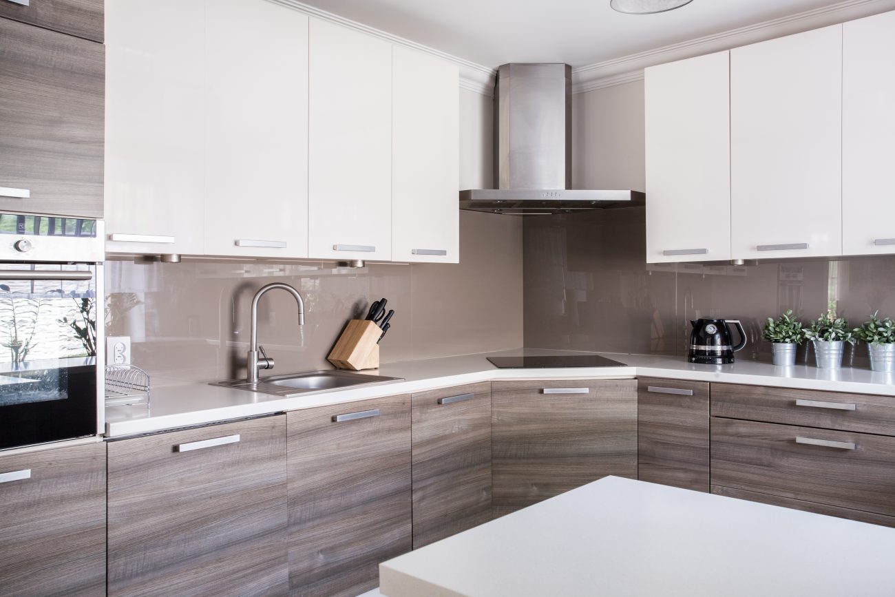 Modern kitchen with brown faux wood and white cabinets, stainless steel cooker hood in the corner and buckets of sage on the countertop