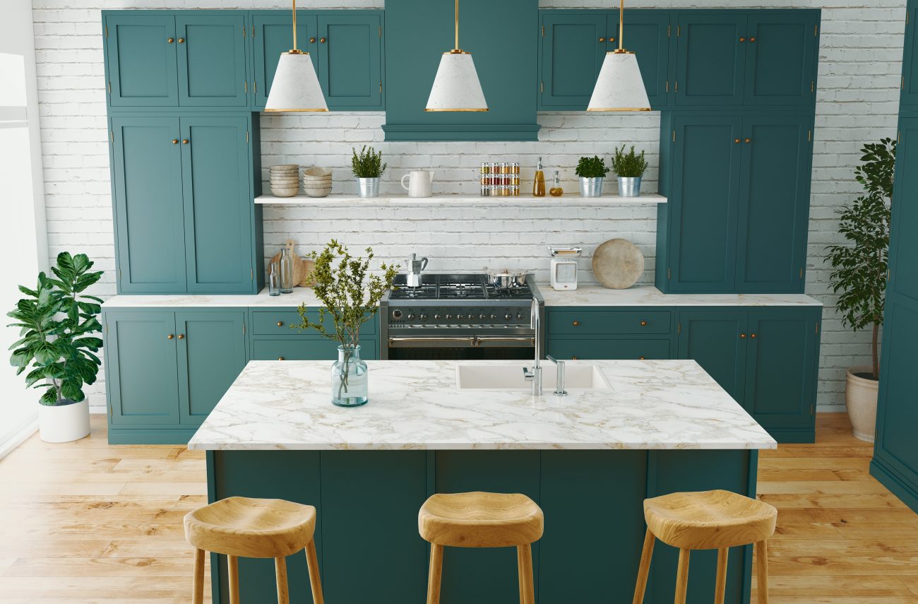 In a modern kitchen, teal green cabinets and island, white brick wall, pale wood counter stools and kitchen tree in the corner of room