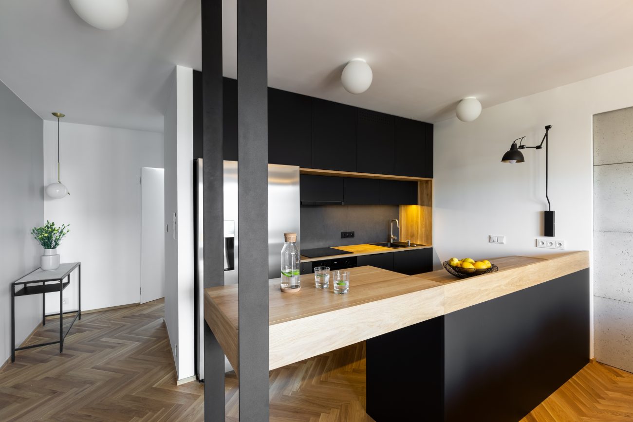 Black peninsula in a modern kitchen with wood countertop and herringbone marquetry floor