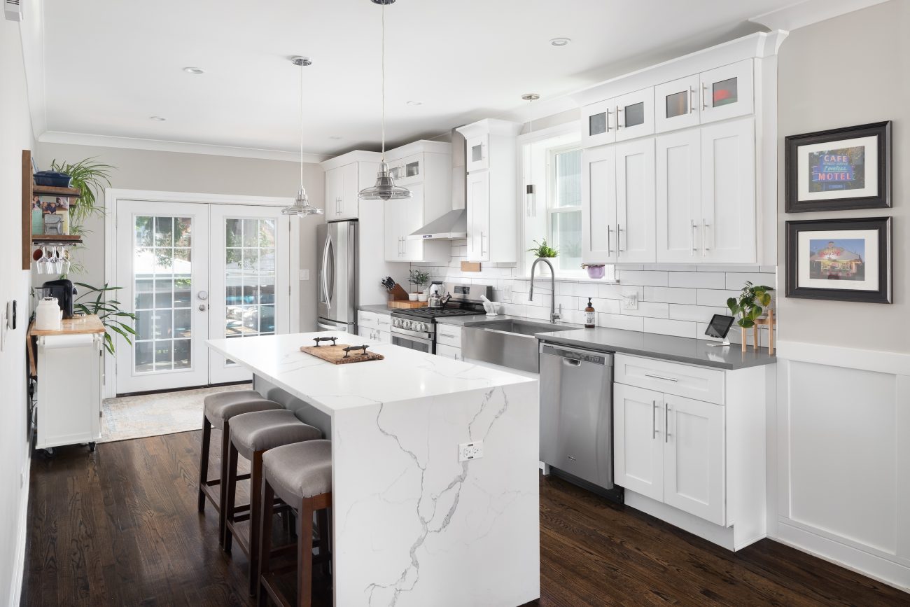 White modern kitchen with a waterfall marble island, stainless steel appliances, and hardwood floor