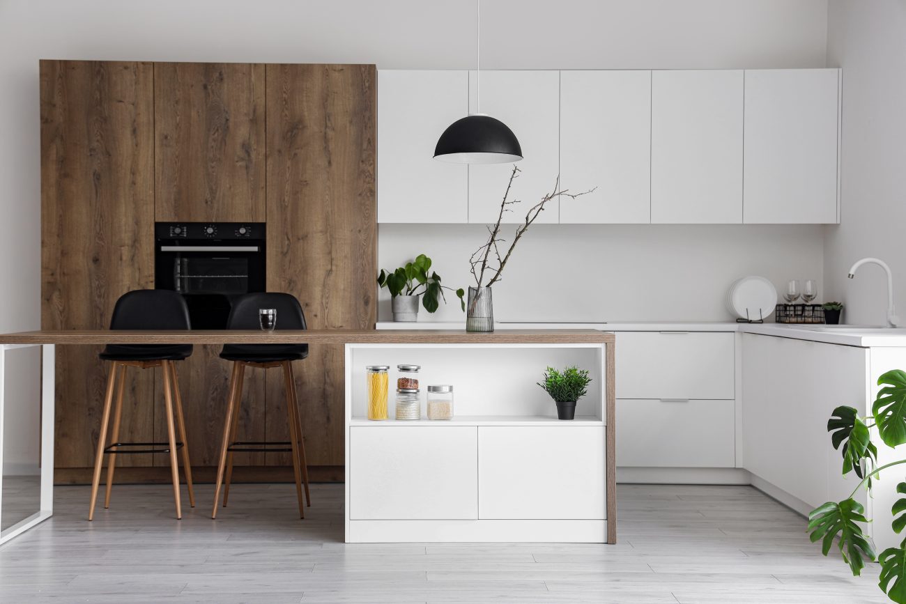 Modern kitchen with small island, adjoining two-seat dining area, built-in oven and white cabinets