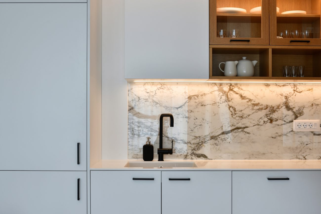 Marble backsplash and diffused lighting under cabinets in a modern kitchen