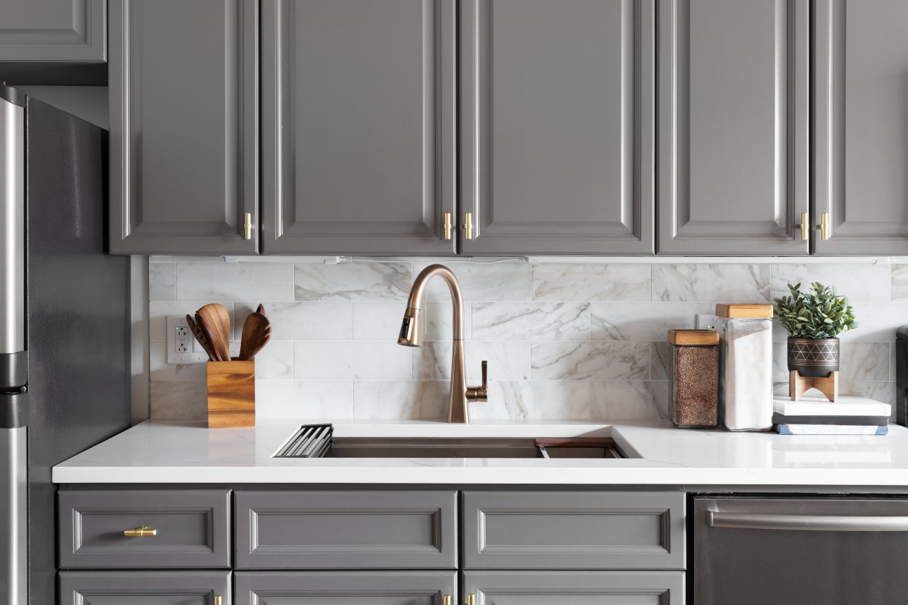 In a modern kitchen, grey Shaker cabinets, rose gold faucet, marbled backsplash