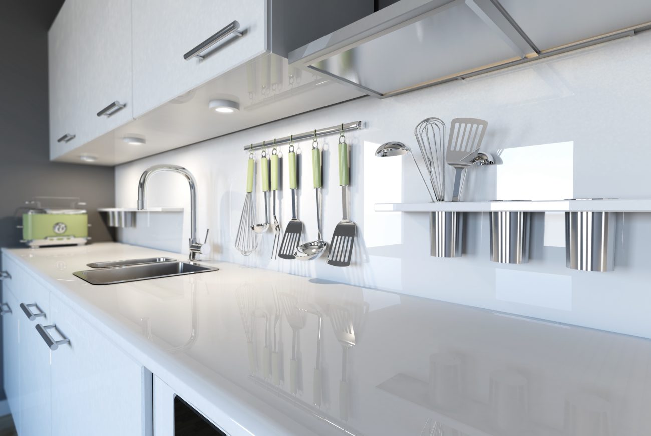 Kitchen utensils with green handles hang on the backsplash of a modern kitchen, with cabinets highlighted by chrome handles