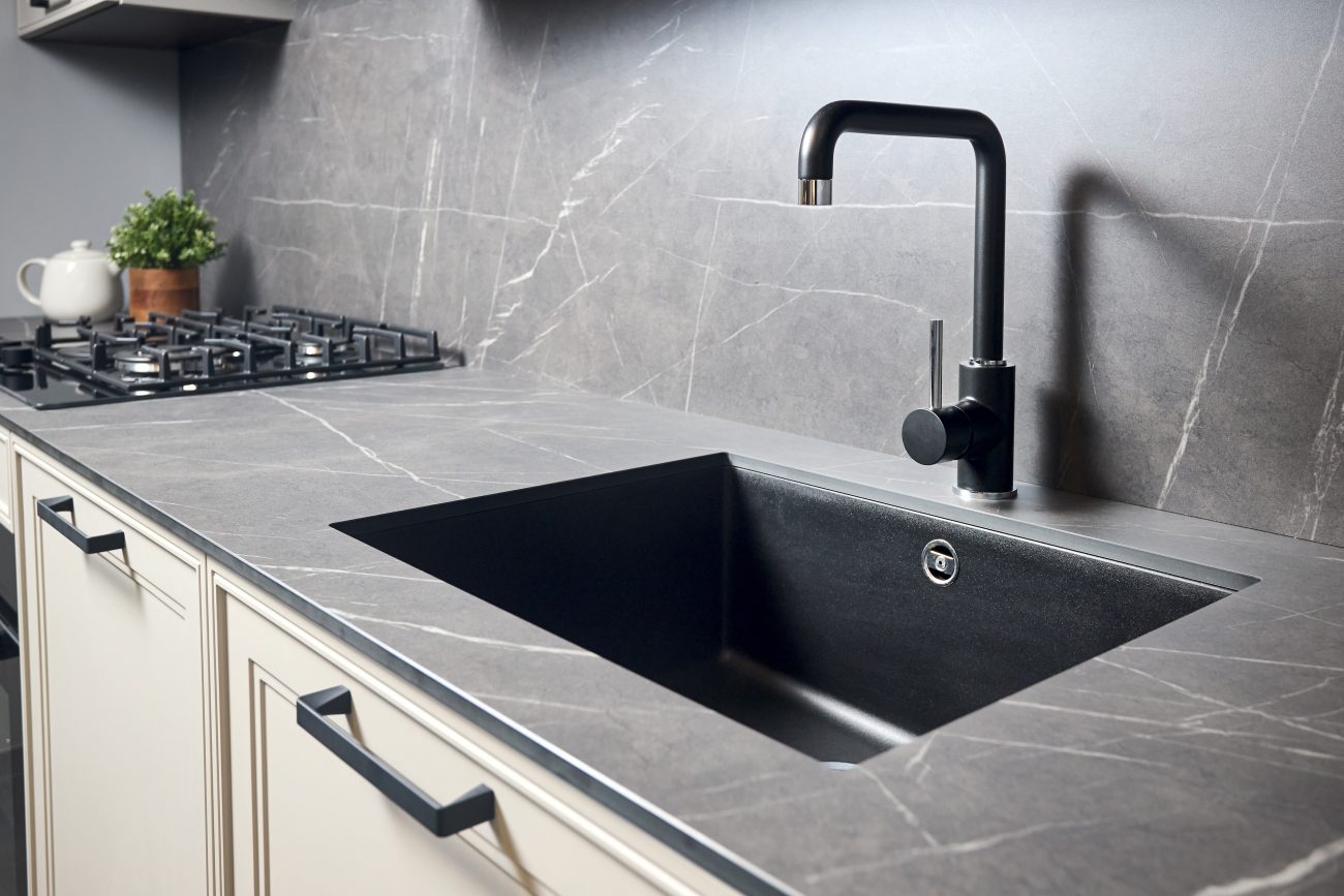 Kitchen undermount sink with black rectangle matte sink tap, gas oven, dark grey marbled countertop and backsplash