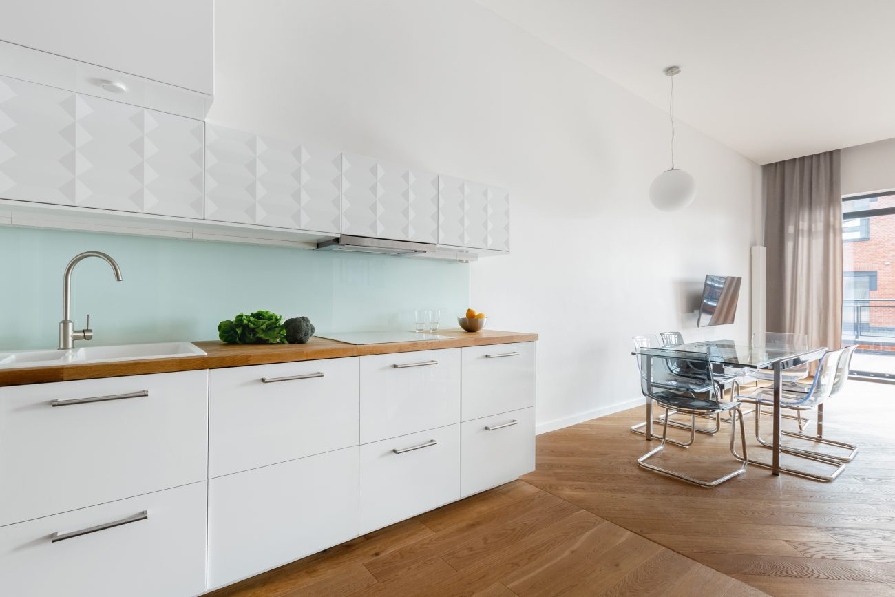 Powder blue backsplash in a modern kitchen with white cabinets, wood countertop and floor