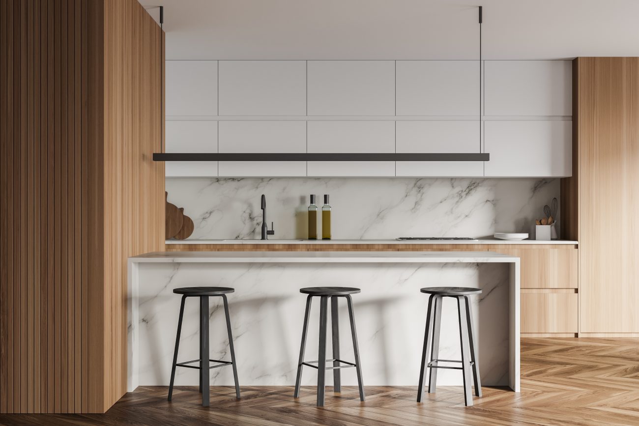 Herringbone marquetry floor in a modern kitchen with marble peninsula and pale wood cabinets