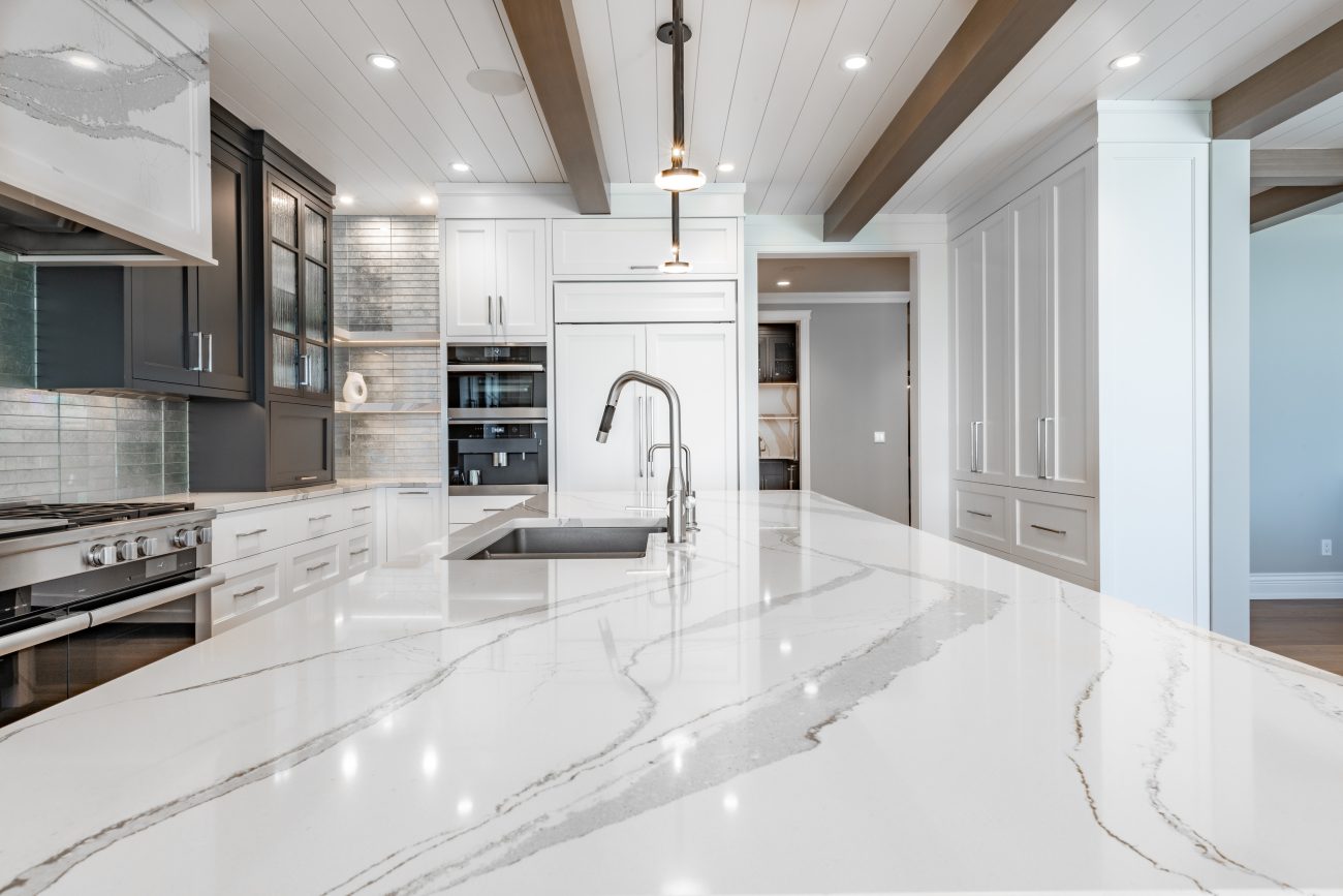 Shiplap ceiling with wood beams in a kitchen with huge marble island and black and white cabinets