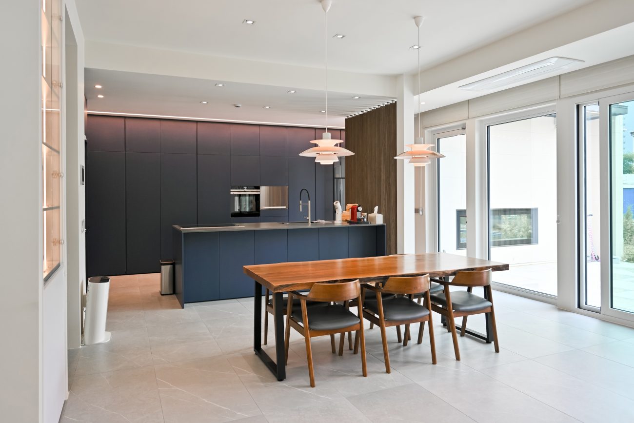 Teak dining set, ink-blue kitchen cabinets and island, and sliding doors in an open-plan space