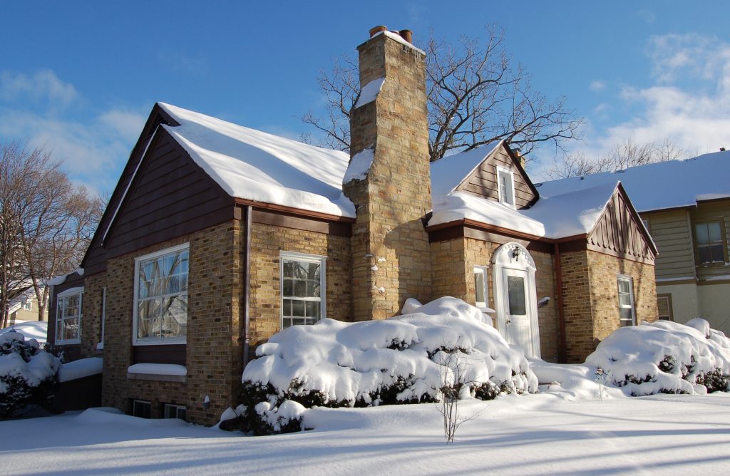 Gabled house and chimney built with bricks, with bushes and snowy ground