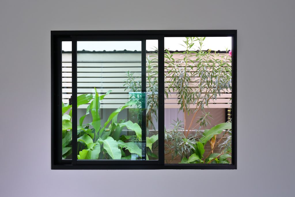 Fenêtre coulissante à cadre noir, ouverte avec vue sur une maison et de la végétation tropicale