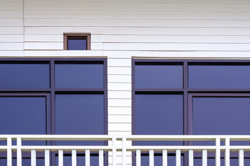 Vue extérieure d’une maison à revêtement blanc, balustrade blanche à barreaux et fenêtres à cadre noir de type industriel, garnies de verre teinté gris foncé