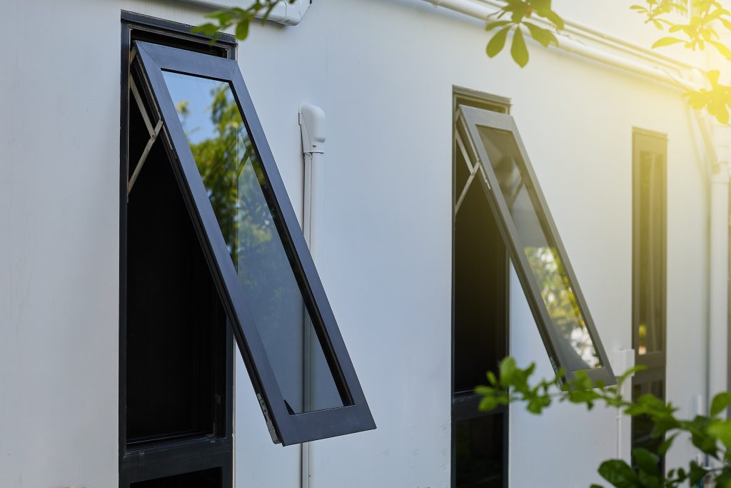 Two awning windows with black aluminum frames, on a light grey facade