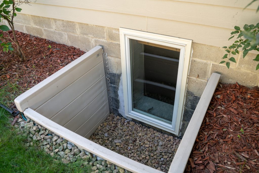 Vertical basement window, serving as an egress, with a flower bed lined with gravel and red mulch