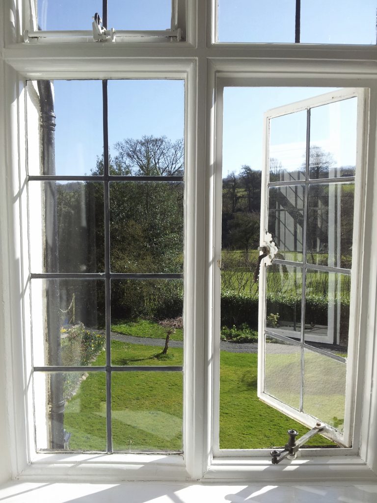 Two casement windows with mullions, one opened on a sunny countryside view