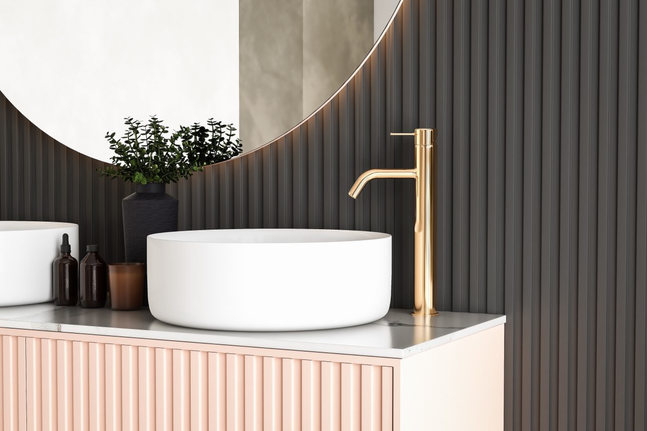 Bathroom with black wall and vertically fluted beige-pink cabinet door, two round white porcelain basins, brass hardware, and large round mirror