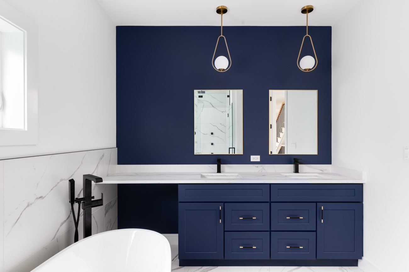 Luxurious bathroom with an indigo-blue accent wall and storage unit, two rectangular mirrors, two built-in sinks, and two contemporary design lights with a white opaque globe