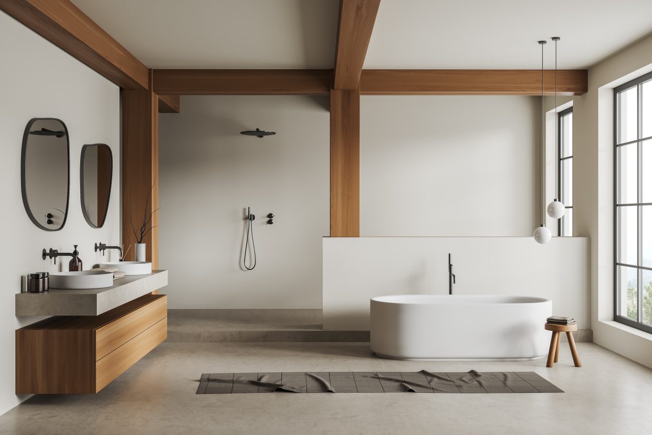 Large white bathroom decorated with beams and a floating wooden storage unit, two porcelain basins, two fluid-shaped mirrors, freestanding oval bathtub, wooden stool, bath mat, and paned windows