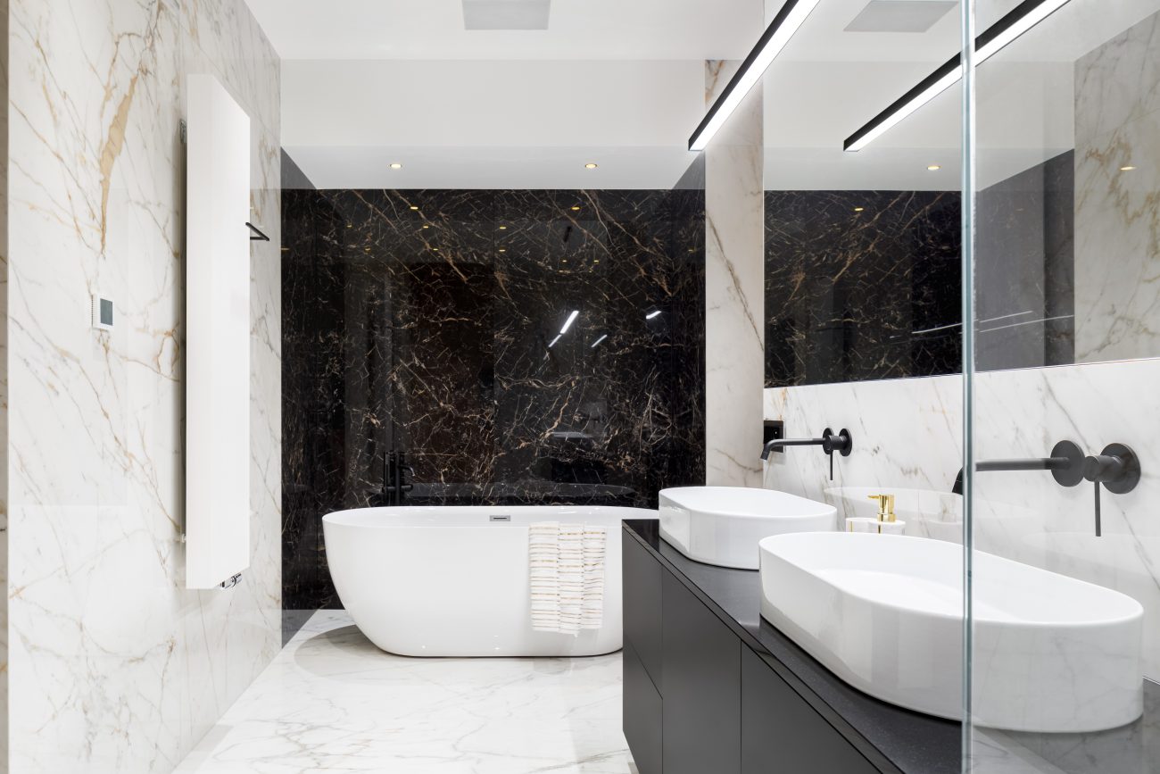 Luxurious bathroom with white and black marble walls, a large mirror above a vanity with two oval basins, a freestanding white bathtub with a towel