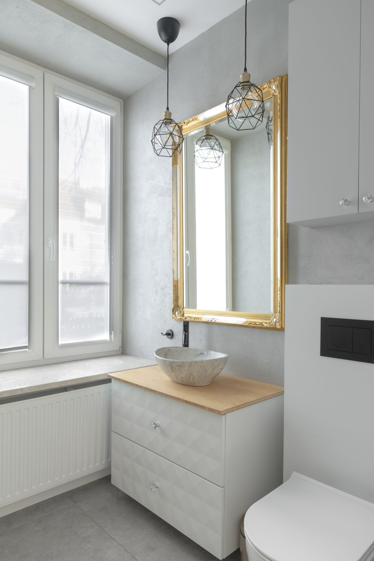 Marble basin on a wooden countertop vanity, ornate gold-framed mirror, two industrial-style pendant lights, and casement windows