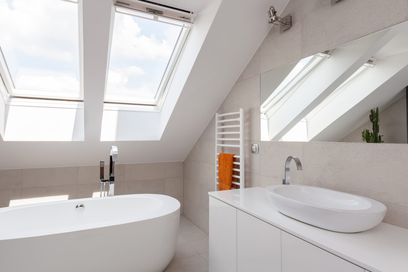 Bright bathroom installed under the eaves, with an openable sloped skylight, bathtub, basin, white cabinet, towel rack with orange towel