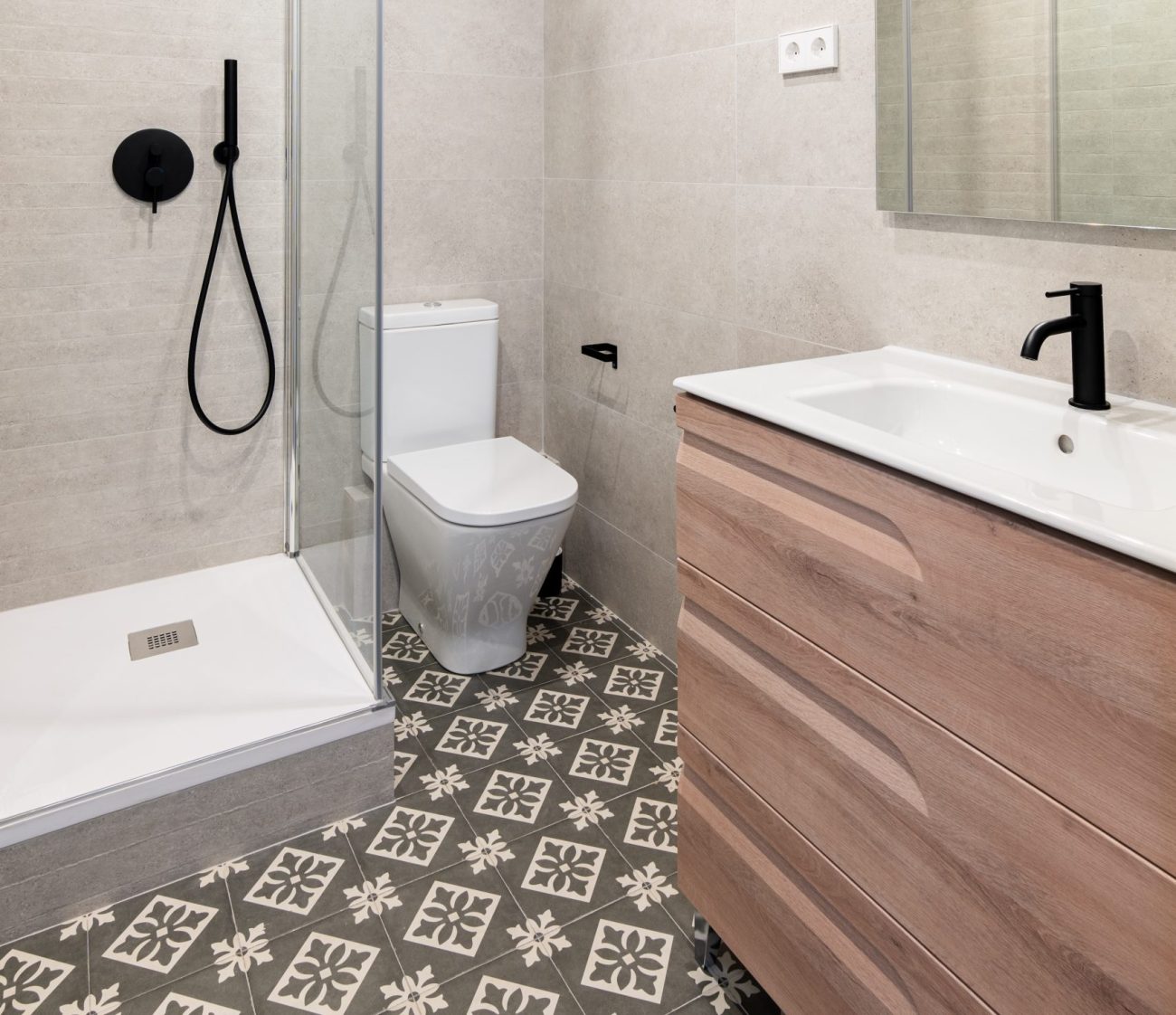 A small bathroom with corner shower, toilet, rosewood-coloured vanity, and geometric patterned floor tiles