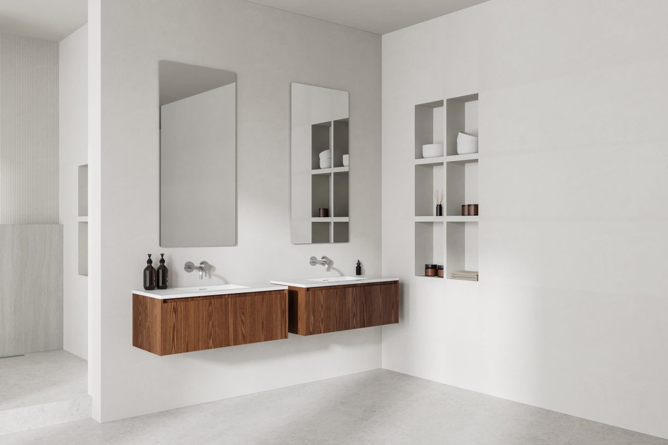 In an all-white bathroom, two dark wood floating vanities with built-in white basins, two tall mirrors, wall niche with candles, and reed diffuser