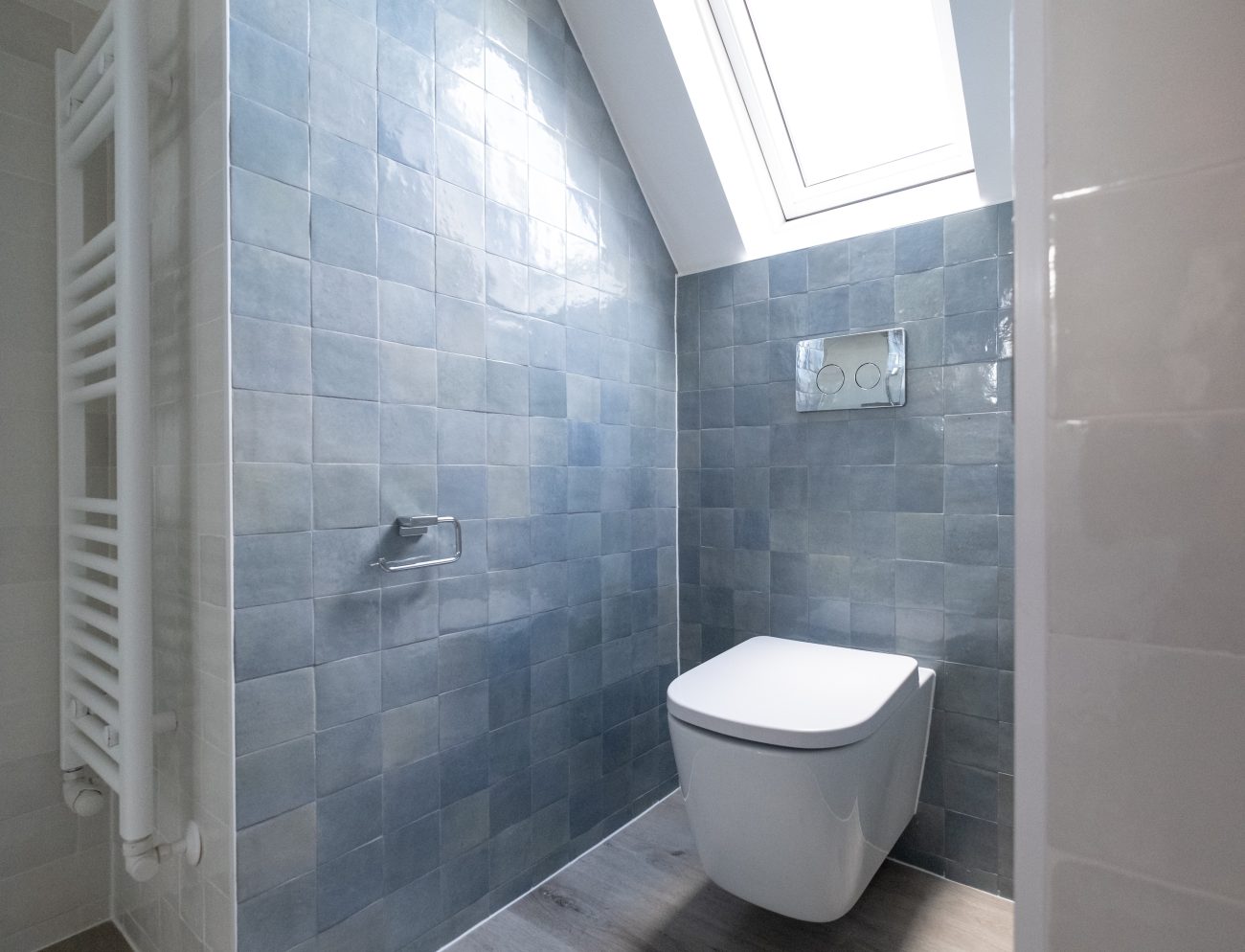 Bathroom with sky blue zellige tile walls, a white wall hung toilet, a skylight, and a heated towel rack