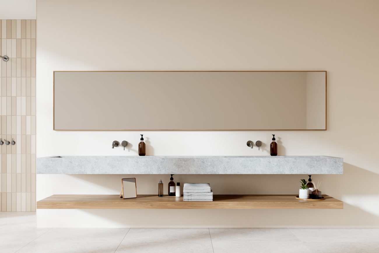 In a luxurious minimalist bathroom, a light grey marble floating countertop with two sinks, a light wood floating shelf with towels and beauty product bottles, and a large rectangular mirror