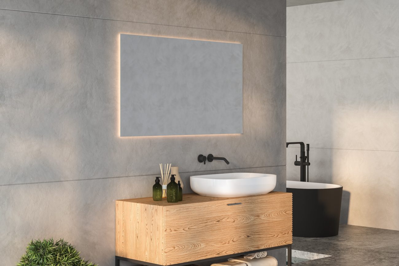 Luxury bathroom with cemented walls, ribbed wood-effect vanity with a square porcelain basin, green glass bottles, freestanding black bathtub, and backlit frame