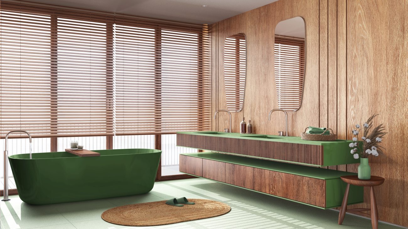 Salle de bain luxe de style japandi, avec accents de bois sur le mur, le panneau cannelé du meuble à deux lavabos encastrés, les armoires du meuble de rangement et le tabouret. Accent de couleur vert gazon sur le dessus des meubles et la baignoire autoportante, plancher vert menthe avec tapis de bain en jute tressée, stores vénitiens devant fenêtres panoramiques