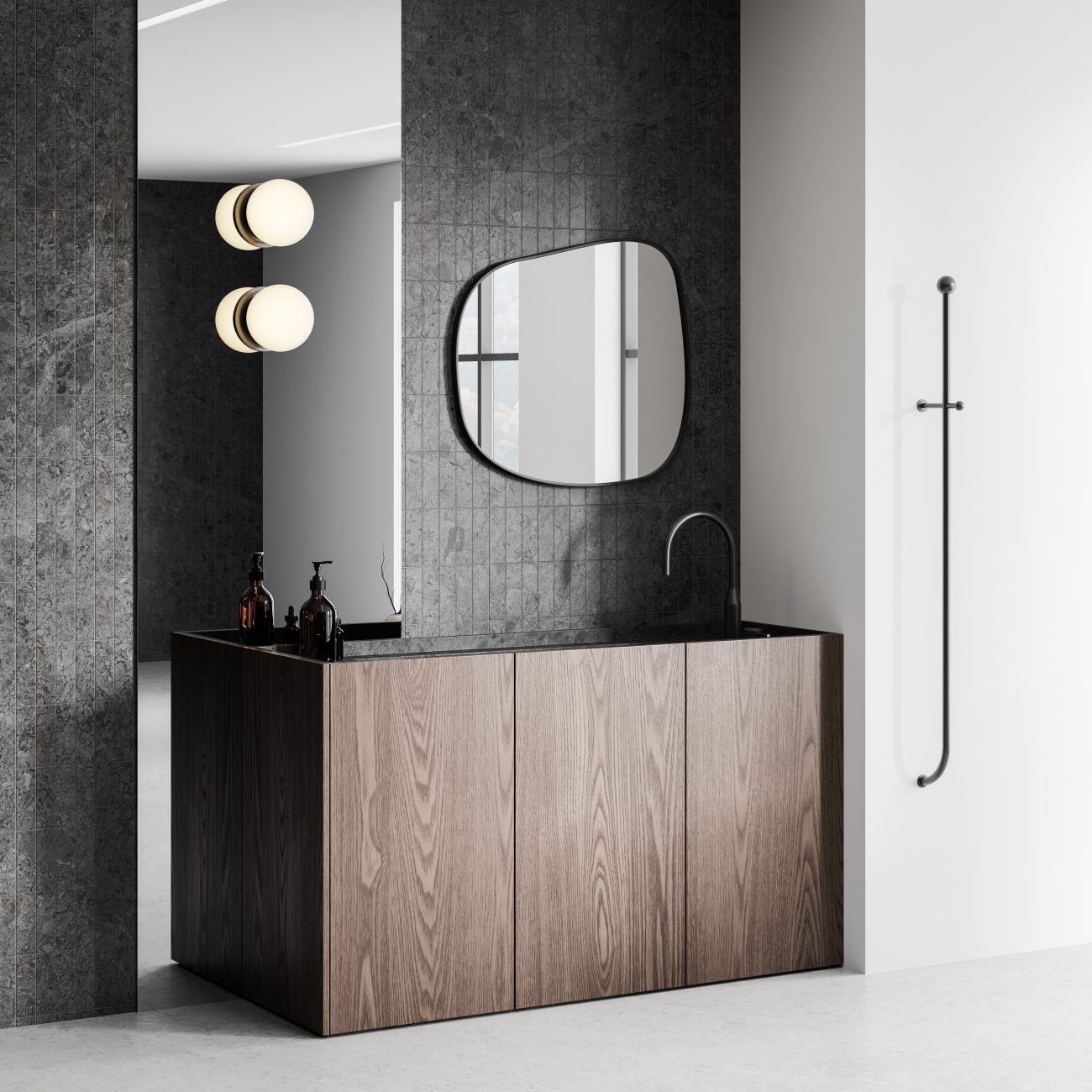 Dans une salle de bain de luxe minimaliste, un meuble-lavabo en bois nervuré muni de portes sans poignées, petit miroir de forme organique sur un mur à carrelage KitKat gris, deux globes lumineux opaques sur pan de mur en miroir