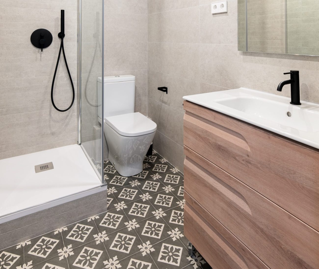 Petite salle de bain avec douche en coin, toilette, meuble-lavabo couleur brun rosé et carrelage de plancher à motifs géométriques