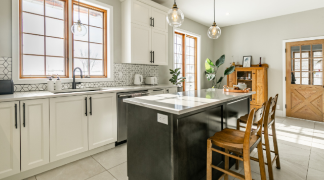 Bright farmhouse kitchen with French doors and windows, subway tile backsplash, black granite island, natural wood chairs and cupboard