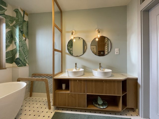 Salle de bain à carrelage noir et blanc, murs vert sauge, papier peint feuillage, meuble-lavabo et claustra en bois