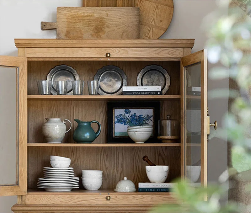 Meuble en bois vitré présentant pots, assiettes, cadre, verres et livres