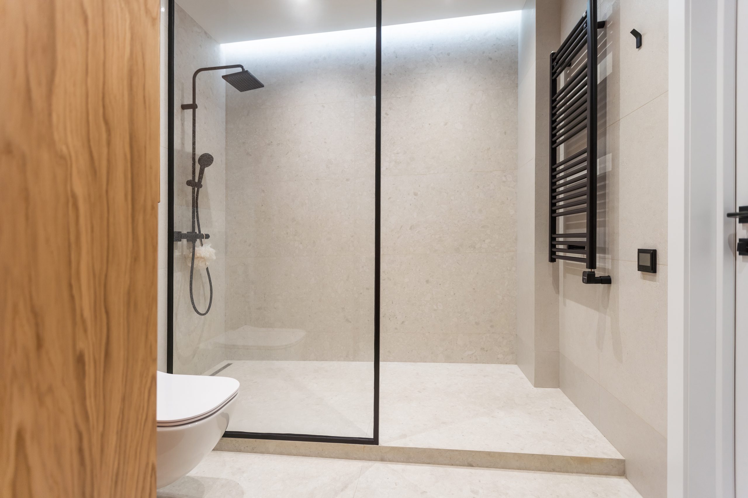 Gray and white tile in the shower and on the floor of a bathroom with glass partition, toilet and towel rail 