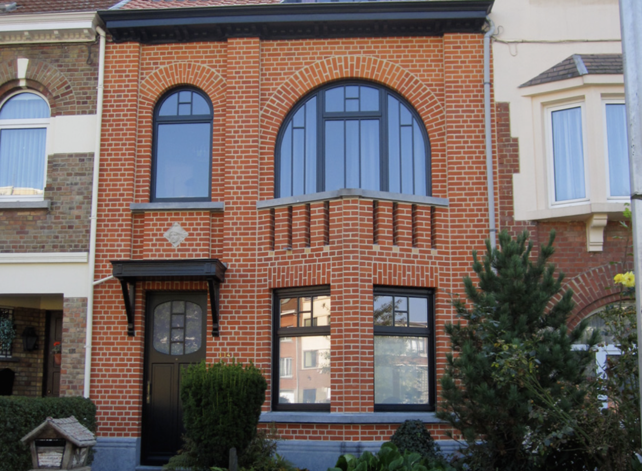 Two-story building with restored red bricks, with half-moon windows and a black door