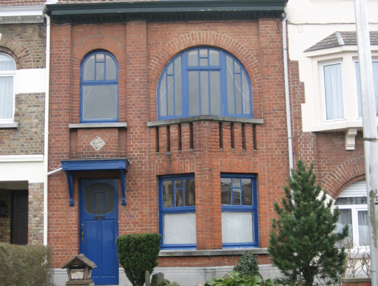 Two-story building with damaged red bricks, with half-moon windows and a blue door