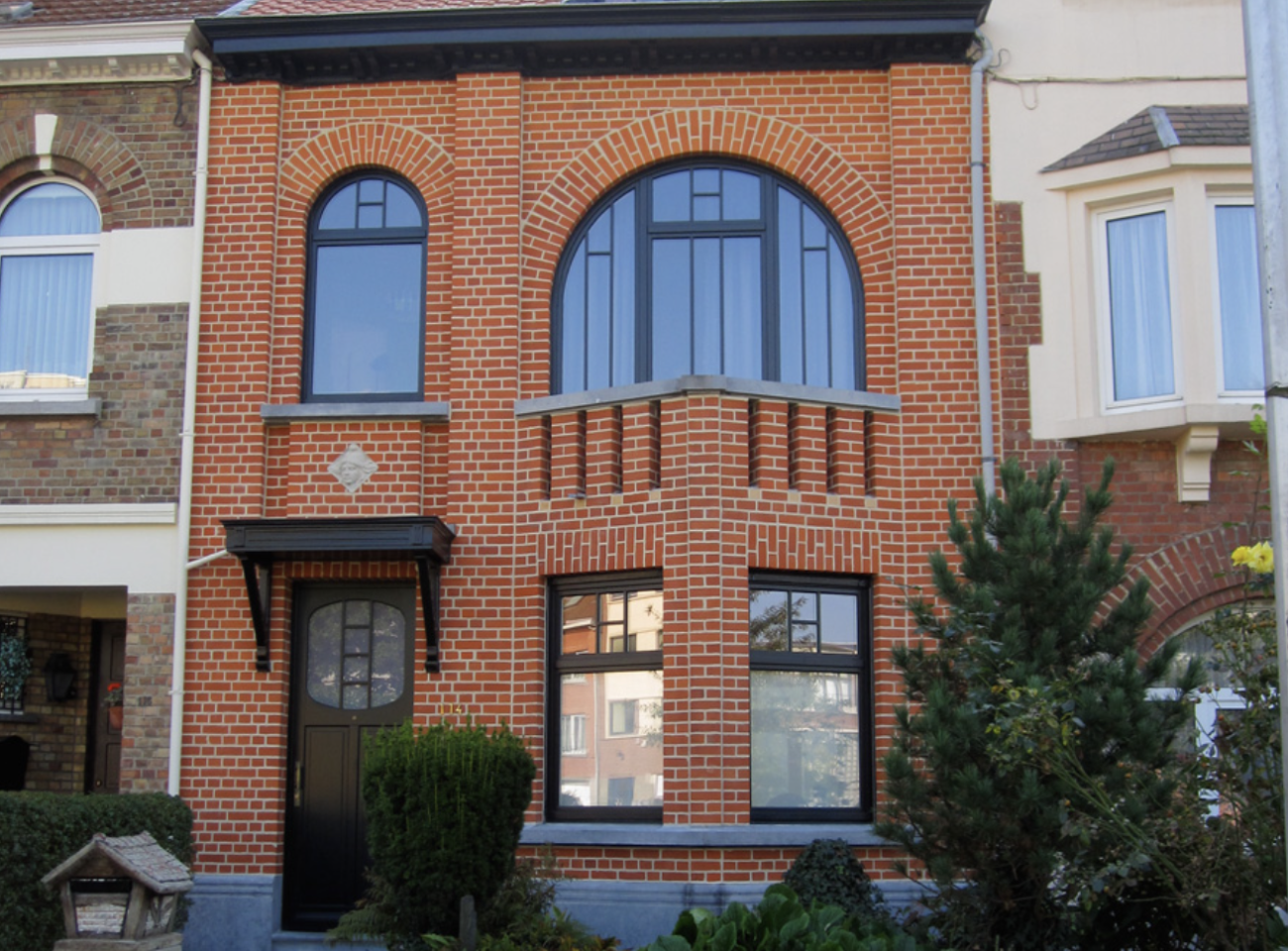 Édifice à deux étages en briques rouges restaurées, avec fenêtres en demi-lunes et porte noire