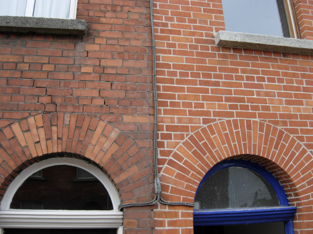 Mur avec fenêtres en demi-lunes, la moitié des briques abîmées et l’autre moitié des briques rénovées par rejointoiement.