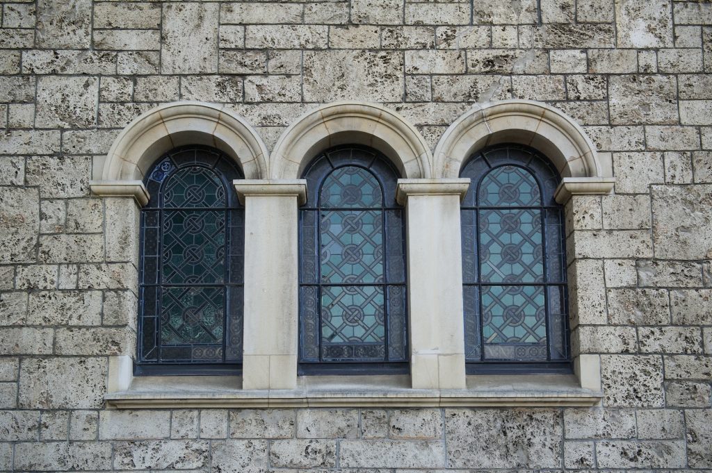 Mur en pierre d’un bâtiment historique et trois fenêtres ornées de vitraux