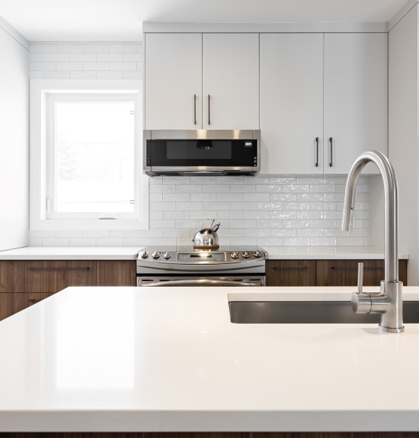 Modern white kitchen with white top cabinets and wood effect laminate bottom cabinets, white ceramic backsplash and island with white stone countertop.