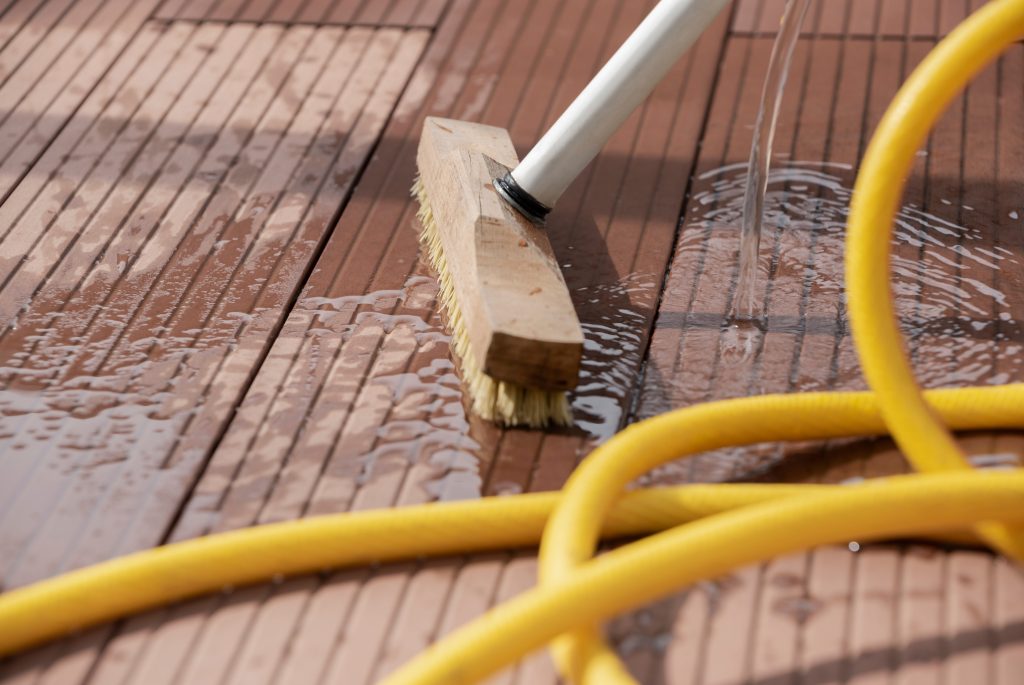 Scrubbing brush and water hose during cleaning of a composite deck floor